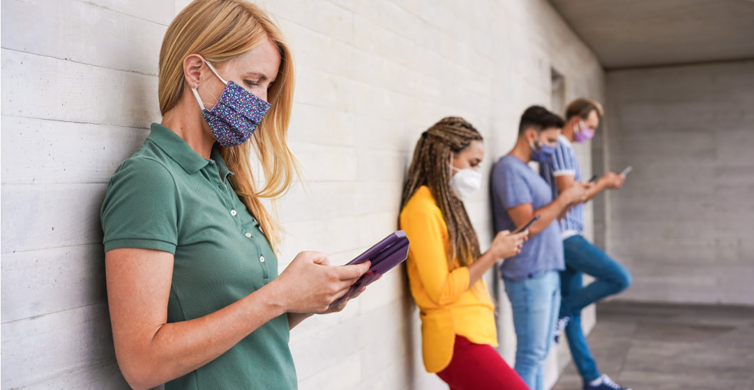 Gente con mascarilla apoyada en una pared mirando sus móviles